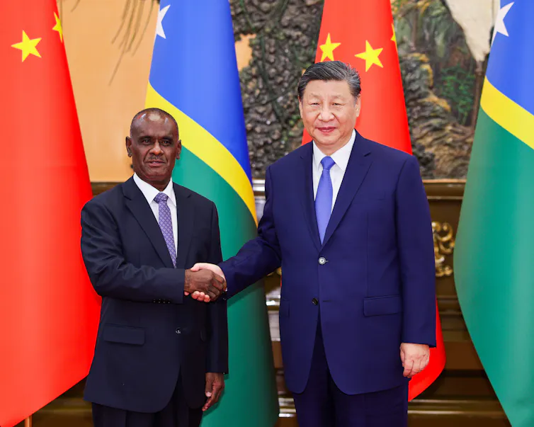 two men in suits shake hands in front of flags