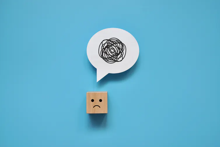 A wooden cube with a frowny face. It has a speech bubble above it that has black scribbles.