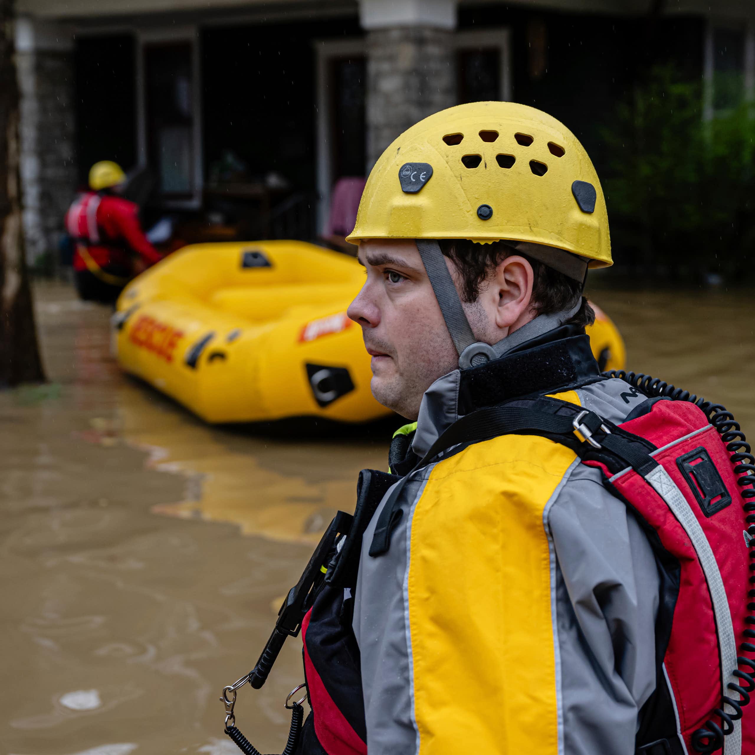 Rescuers with an inflated boat walk in waist-deep water toward older brick houses.