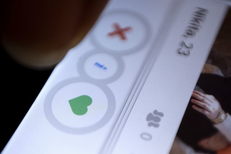 A closeup photo of a dating app displayed on a smartphone with a green heart button and a red X button