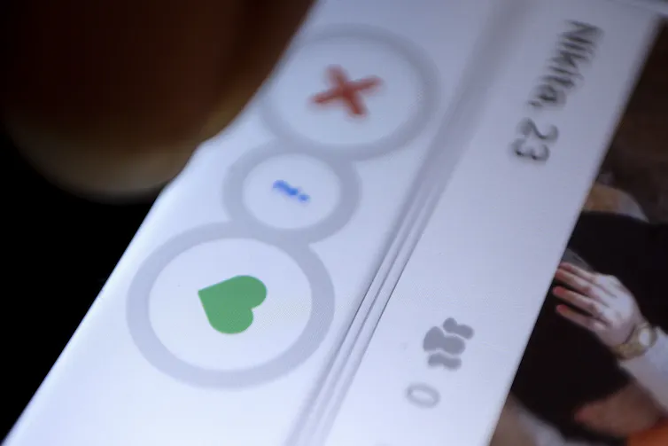 A closeup photo of a dating app displayed on a smartphone with a green heart button and a red X button