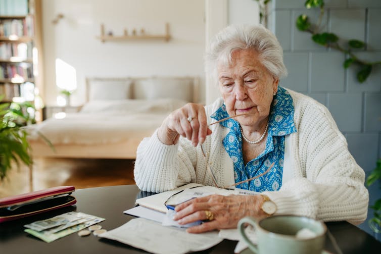An elderly lady sits at a table with papers in front of her.