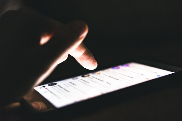 finger hovering over an illuminated smartphone in the dark