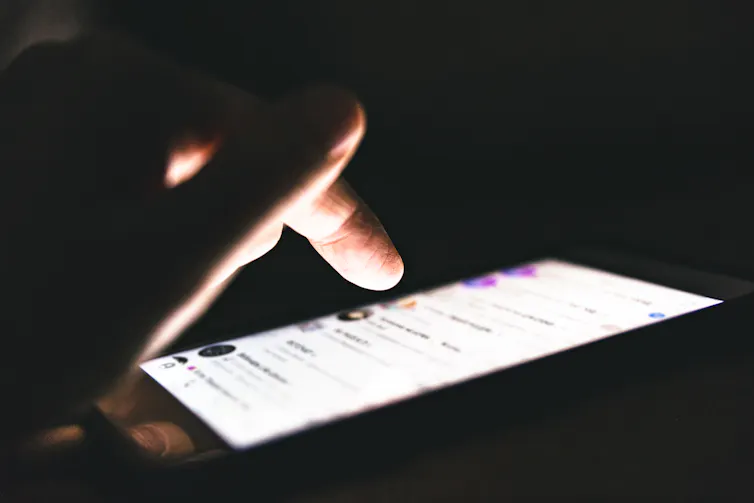 finger hovering over an illuminated smartphone in the dark