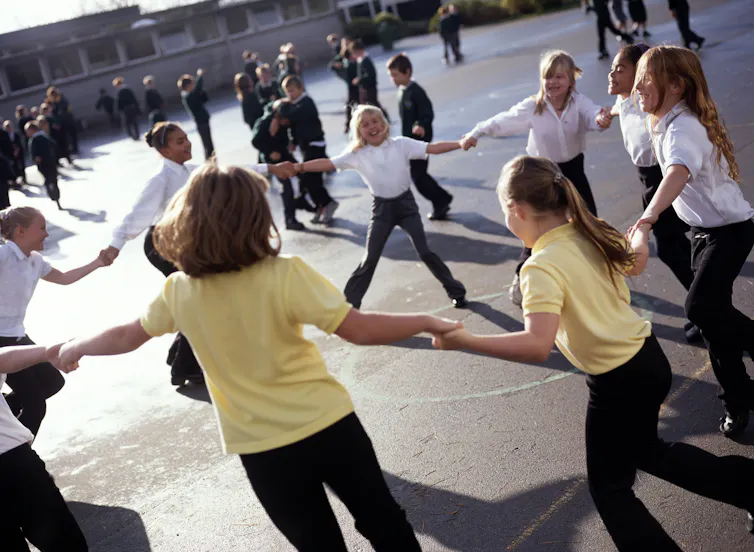 Smiling children playing 'ring around the rosy' in a schoolyard