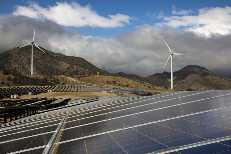 Wind turbines behind fields of solar panels in the mountains.