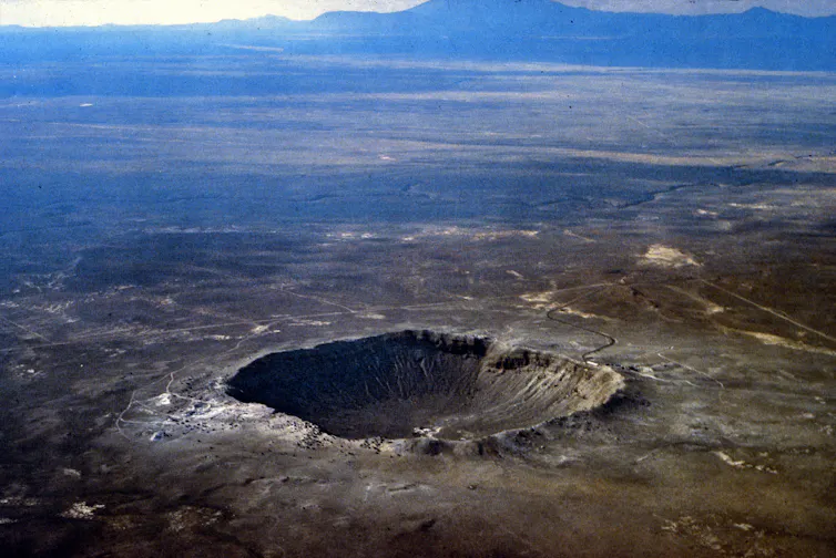 A large crater with a raised rim in the middle of desert terrain.