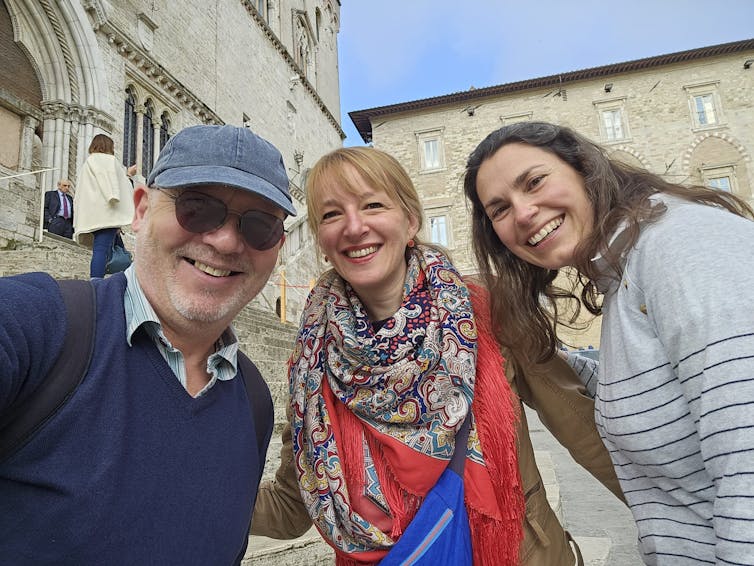 Man with blue hat and sunglasses, woman in colourful scarf and another woman with dark hair standing together in Italian square