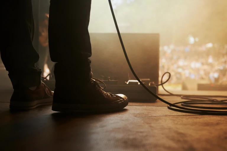 Feet of a musician on stage with the blurry crowd in the background.