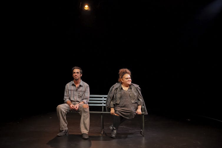 Production image: a man and a woman sit on a bench.