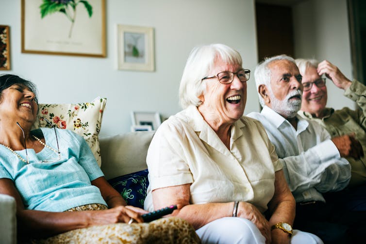 A group of older men and women sit on a couch watching television.