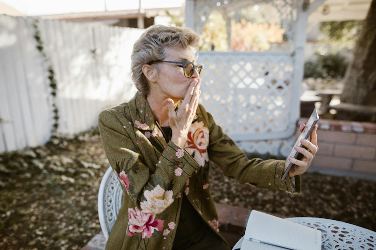 Elderly woman wearing a floral blazer on a video call on her phone.