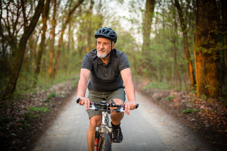Older man riding a bicycle through a forest.