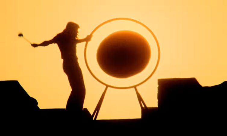 A gong is hit against the setting sun.