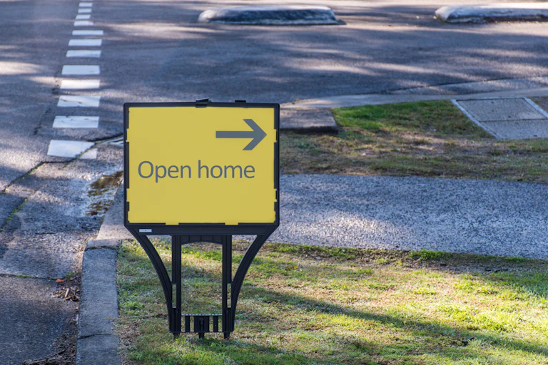 A yellow and black sign on a street that says open home with an arrow pointing to the right.
