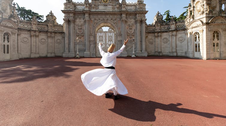 A whirling dervish dressed in white dances in front of a palace.