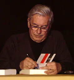 Un hombre firmando un libro sentado a una mesa.