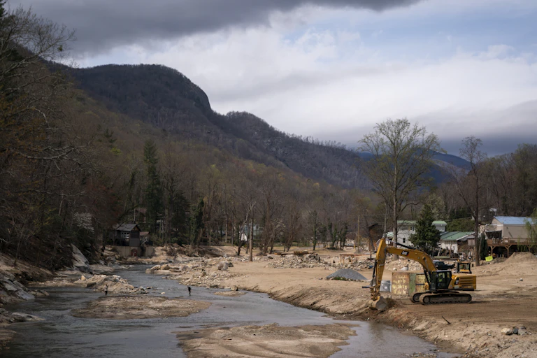 An excavator sits along the Broad River in a landscape scarred by flooding.