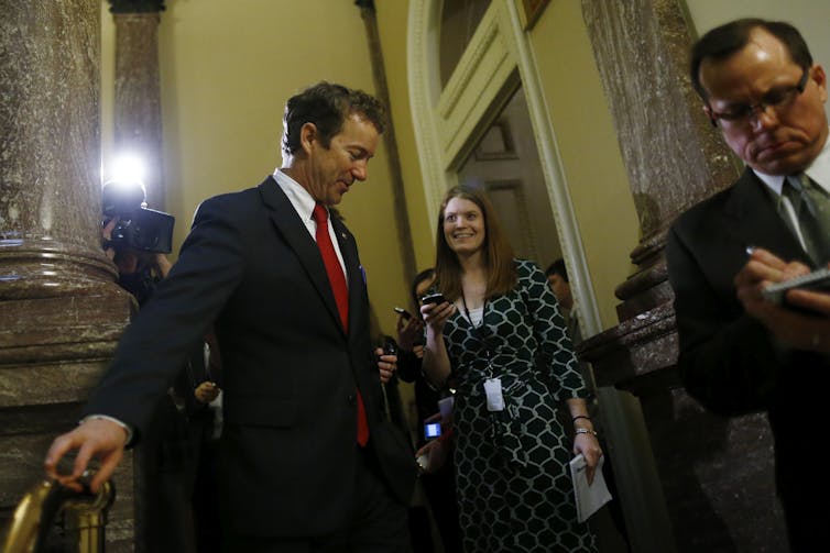 A man dressed in a suit in the U.S. Senate is asked questions be reporters.