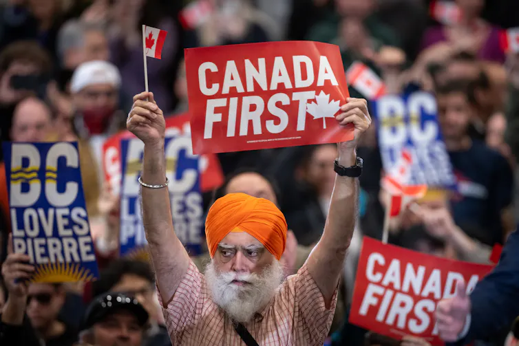 A sikh man wearing an orange tuban holds sign reading Canada first at a political rally