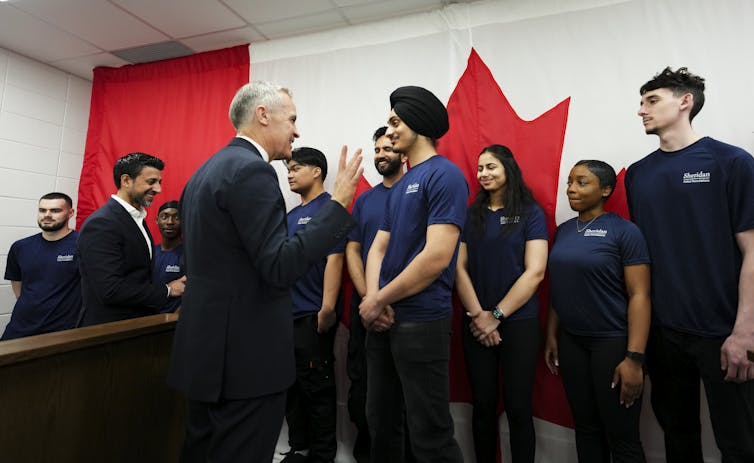 El hombre blanco con un traje oscuro habla sobre el joven hombre aastrico del sur con Turbani. Otros jóvenes se paran en el fondo