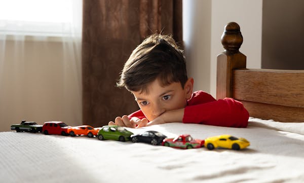 Child looking at colorful toy cars arranged in a line across a table or bed