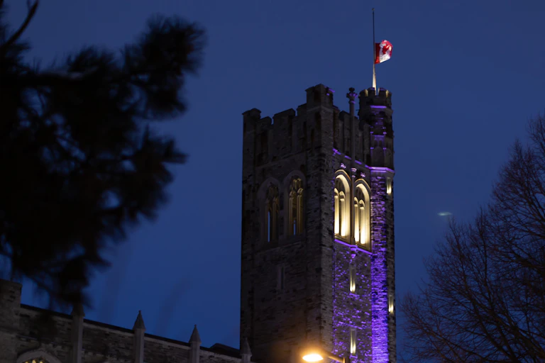 A red and white maple leaf flag against a purple sky and stone building.