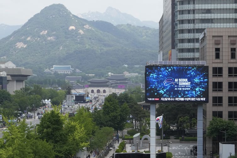 A digital sign advertising an AI conference against a cityscape.