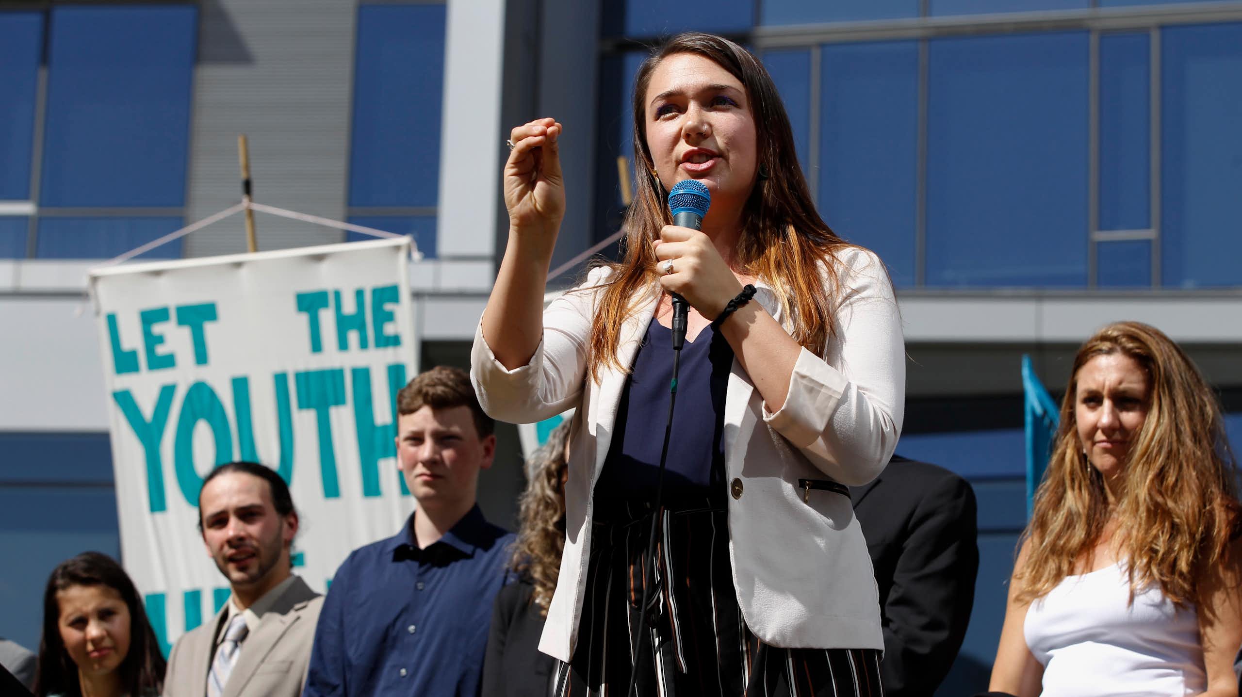 A woman holds a microphone and gestures to a crowd.