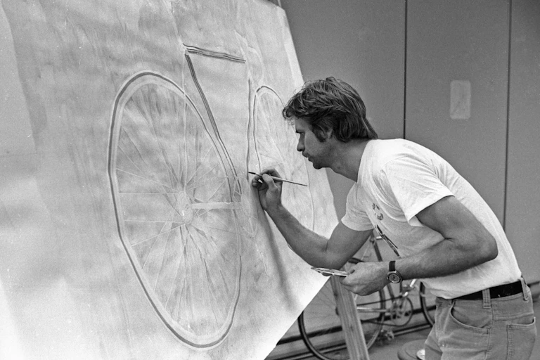 A man standing at an easel drawing a bicycle.