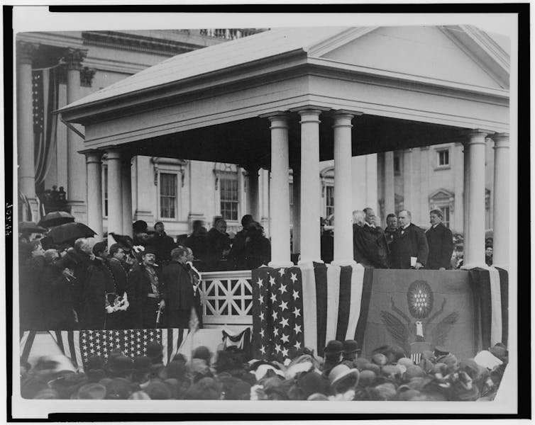 Several men dressed in black stand on a platform decorated with the U.S. flag.