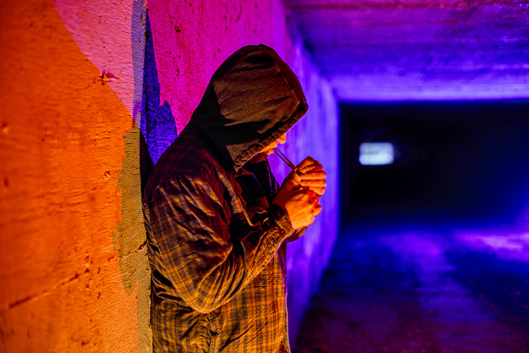 A person wearing a hoodie smoking drugs out of a glass pipe in an underground tunnel
