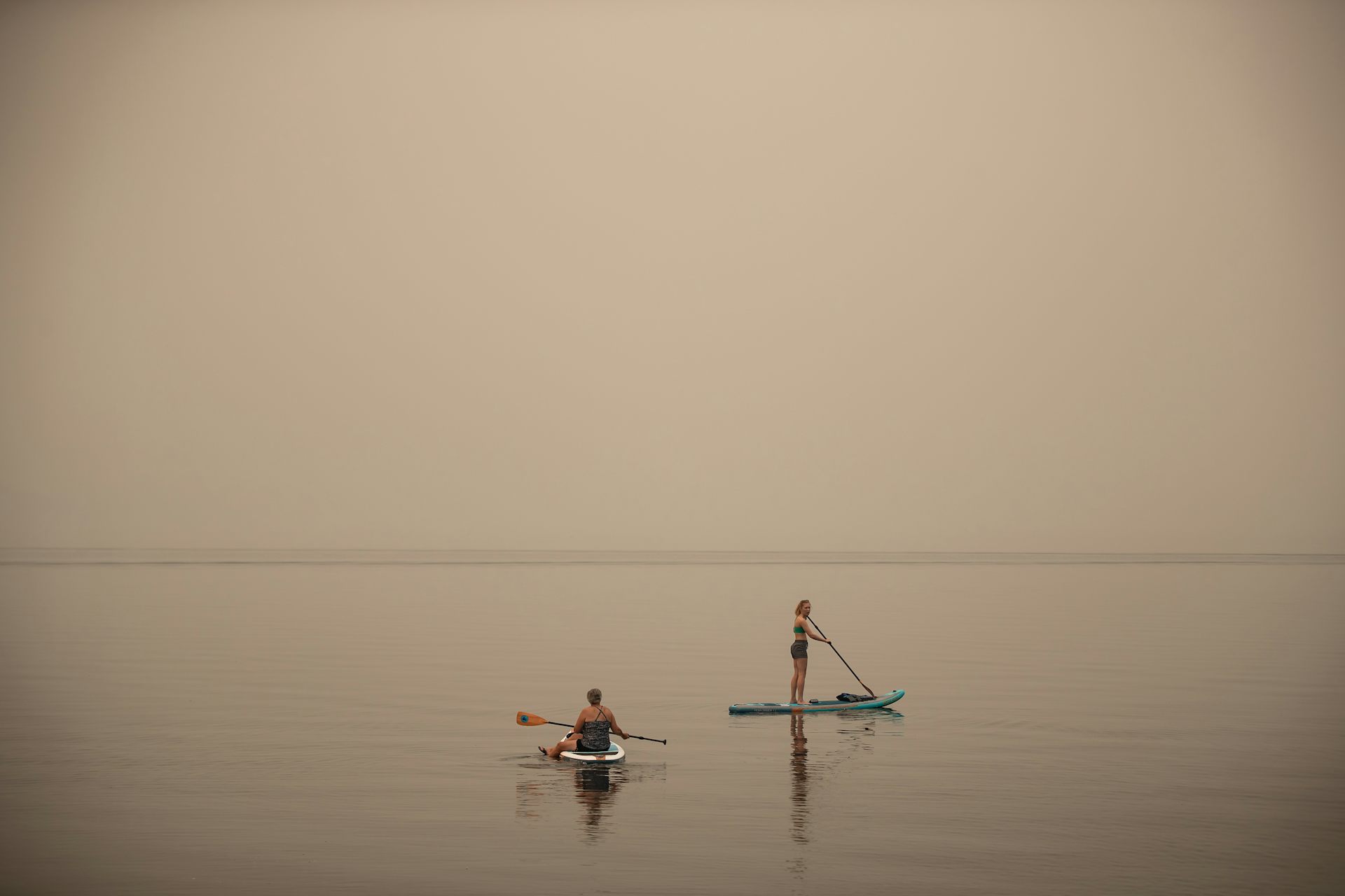 Two women on paddleboards with smoky haze obscuring the horizon