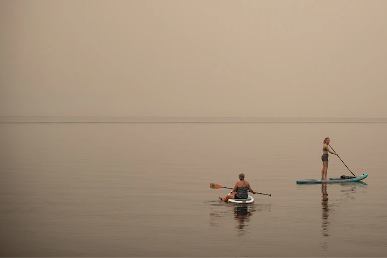 Two women on paddleboards with smoky haze obscuring the horizon