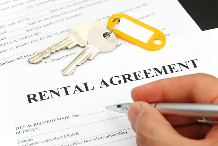 Unidentified hand signing a rental agreement. Keys with yellow tag lying on top