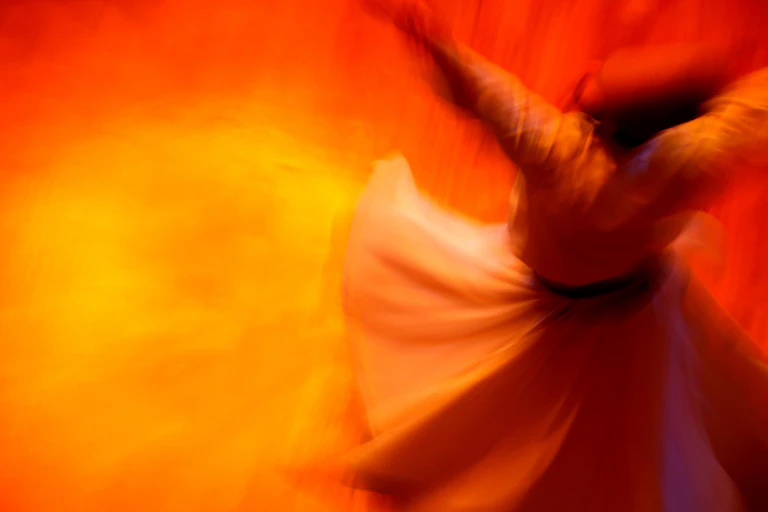 A man in a white gown and hat twirling.