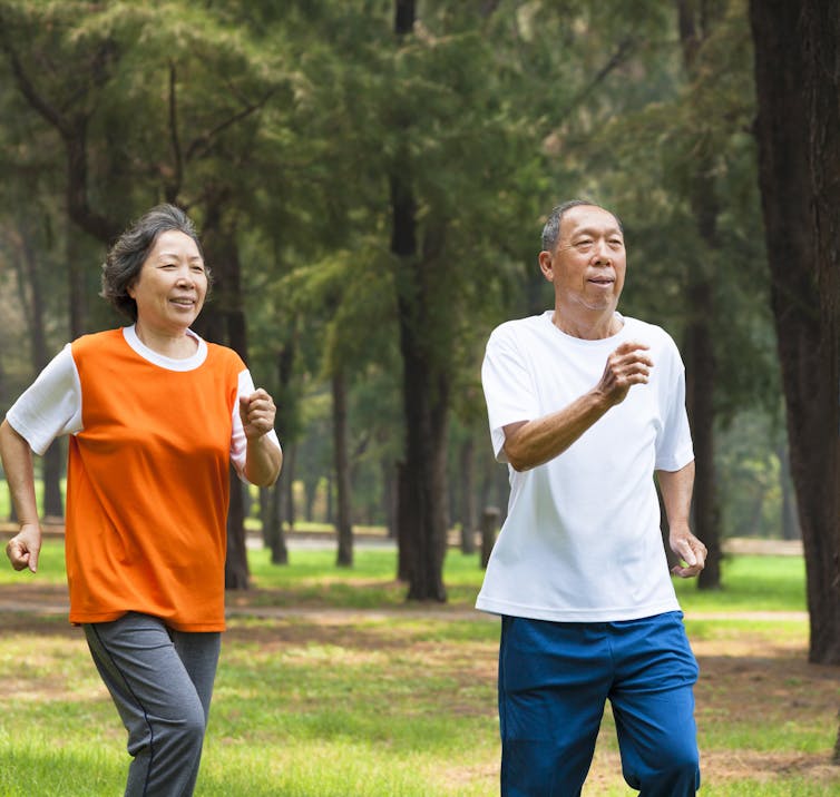 Older man and woman jogging through a park together.