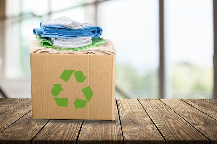 cardboard box full of clothes, green recycling logo, box sat on wooden surface