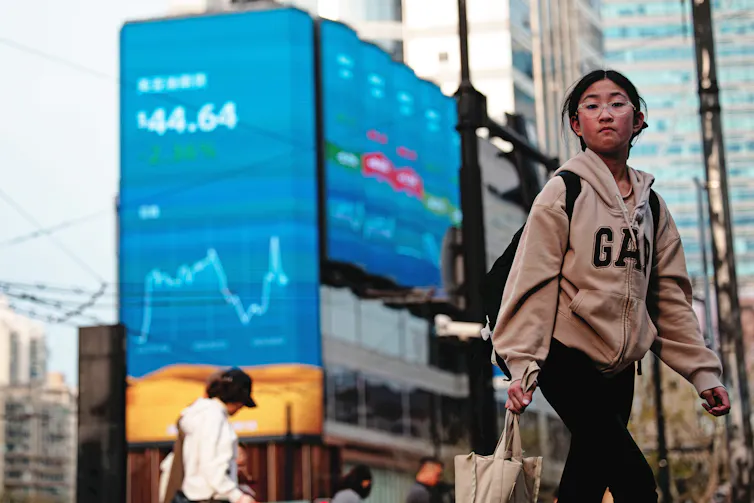 A person walks on a street near screens showing stock exchange and economic data in Shanghai, China.