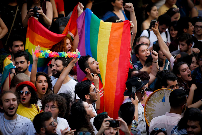 Overhead view of a crowd at a Pride march, a rainbow flag held up by the crowd is the focal point of the photo