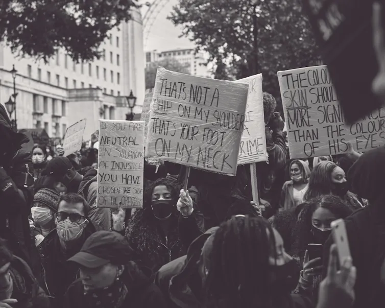 Black and white photo of marchers carrying handmade signs, one reading 'that's not a chip on my shoulder, that's your foot on my neck.'