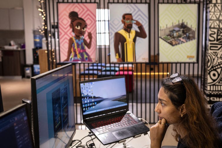 A woman with long hair sits working on her computer in a bright, modern office with two large posters of African animated figures.