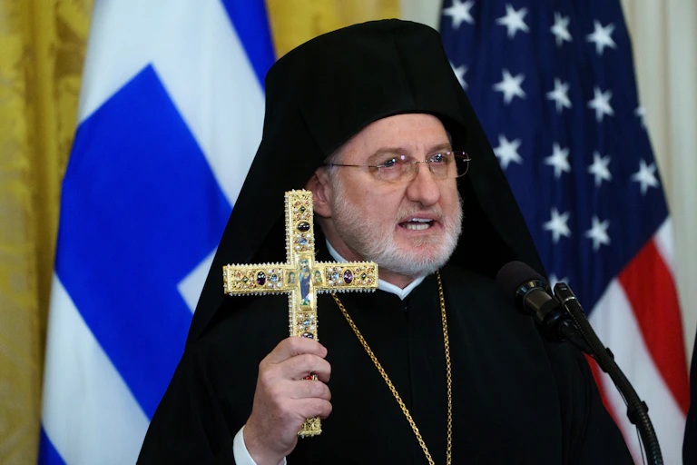 Archbishop Elpidophoros of America holding a gold cross.