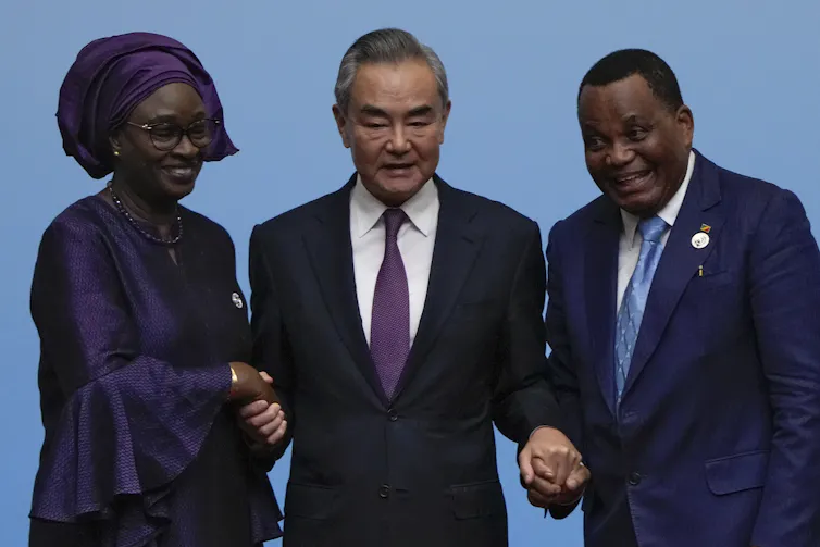 An Asian man stands between a Black woman and a Black man, clasping their hands.
