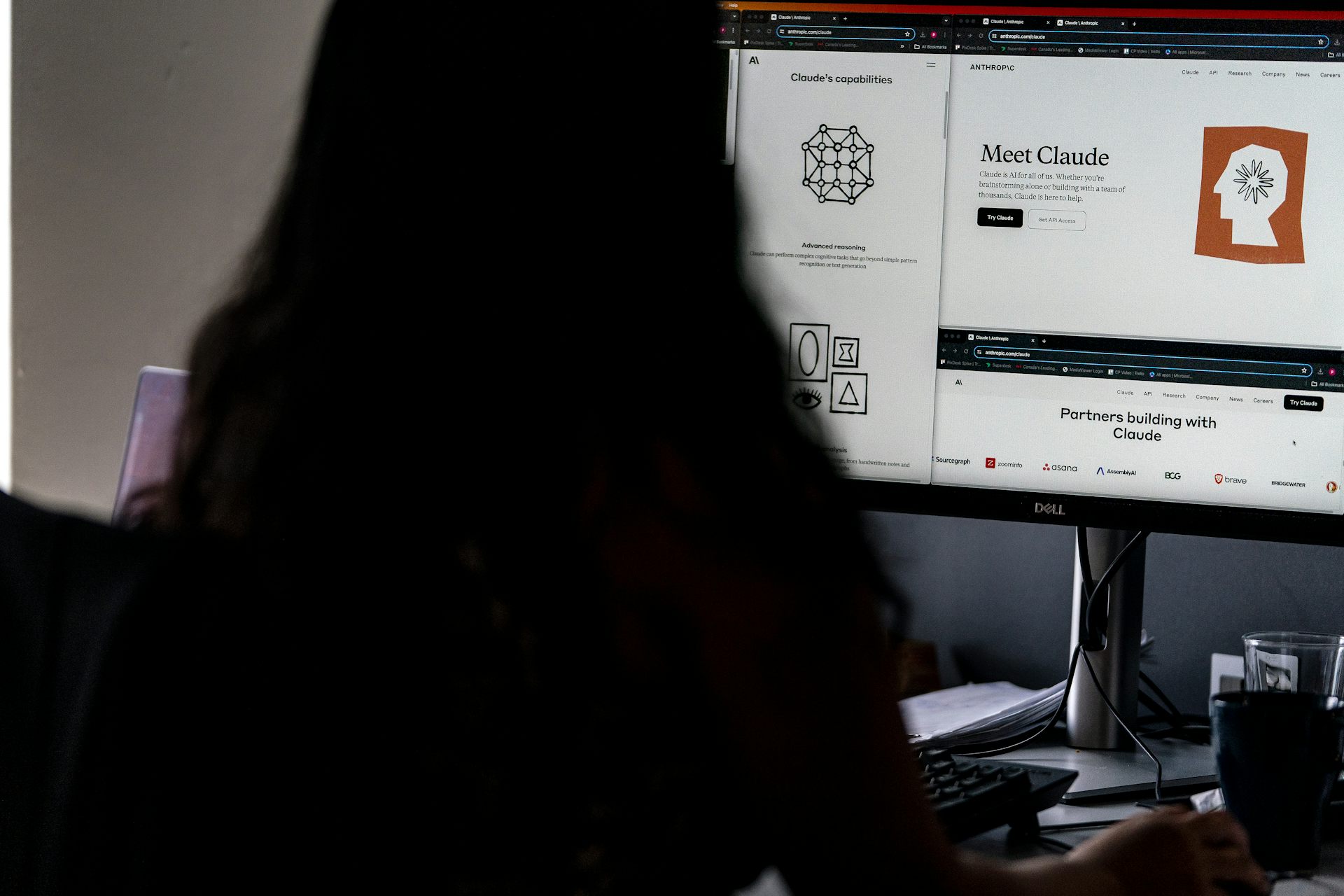 A woman seen from behind, looking at a computer screen displaying elements of the Claude AI