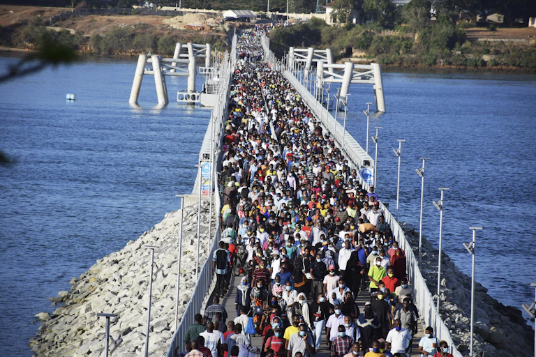 People cross a floating foot bridge crossing a river.