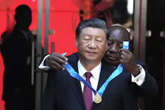 A Black man places a medal around an Asian man's neck.