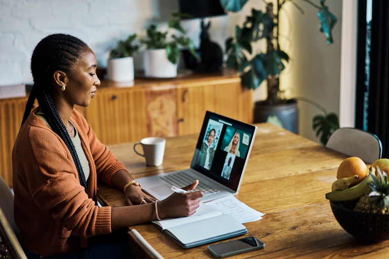 A Black woman participates in a virtual video call on her laptop, with three other individuals visible on the screen.