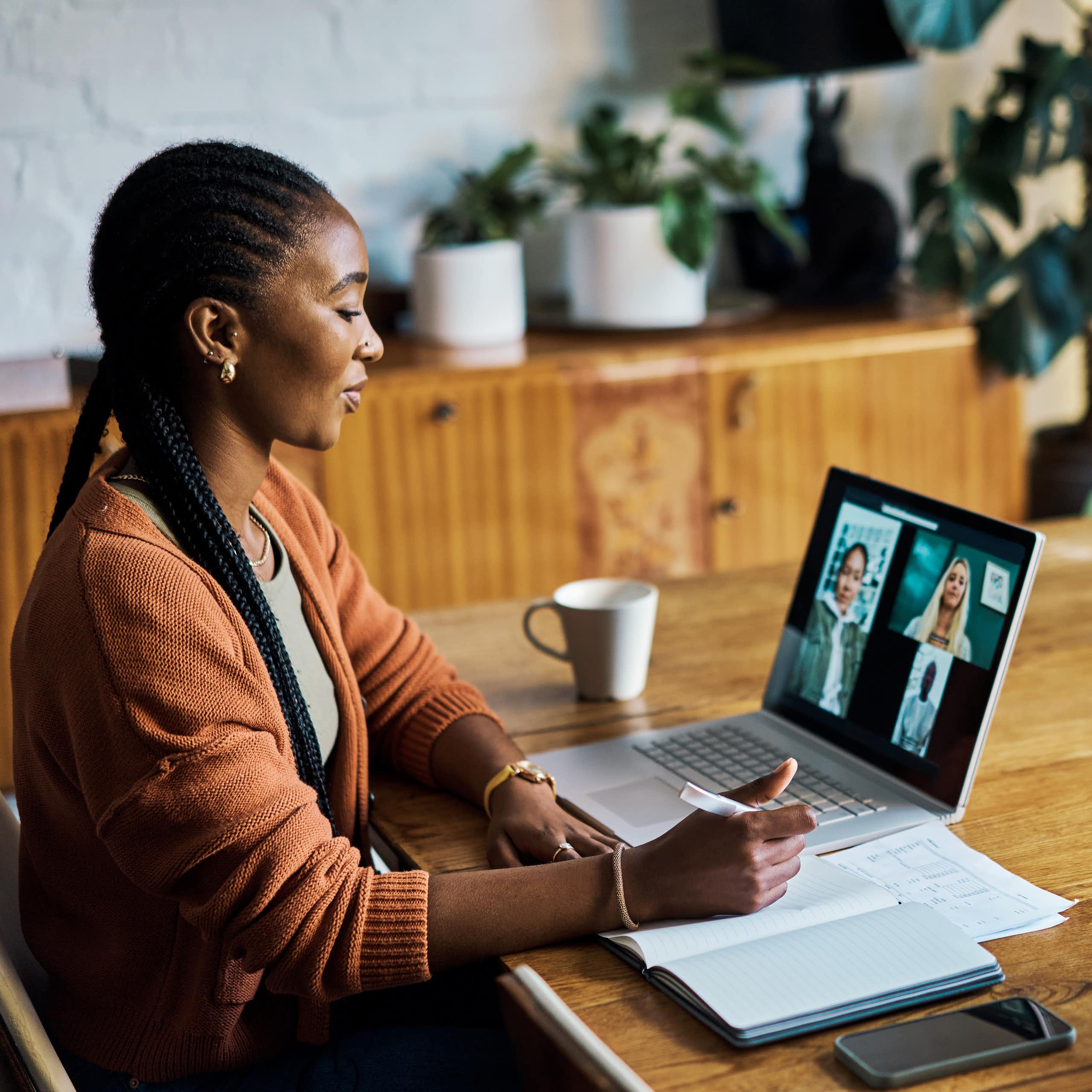 A Black woman participates in a virtual video call on her laptop, with three other individuals visible on the screen.