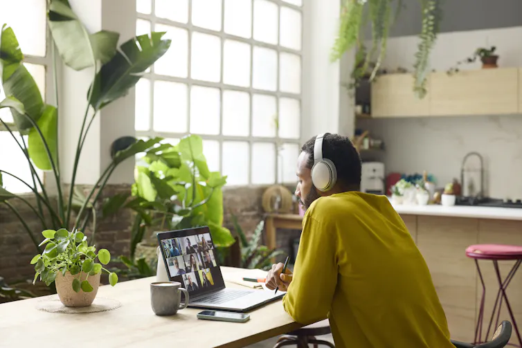 A young man wearing headphones is participating in a video conference on his laptop.